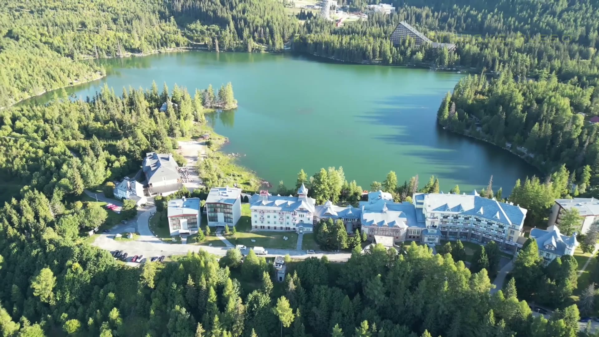 Grand Hotel Kempinski High Tatras beside the green waters of Štrbské Pleso, surrounded by forest