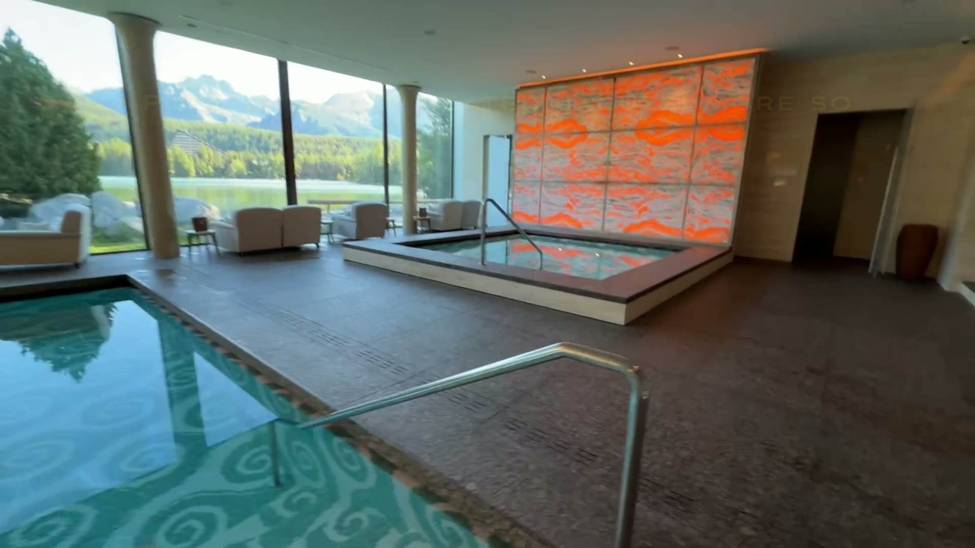 Indoor spa pool and loungers beside large windows overlooking Štrbské Pleso and the mountains