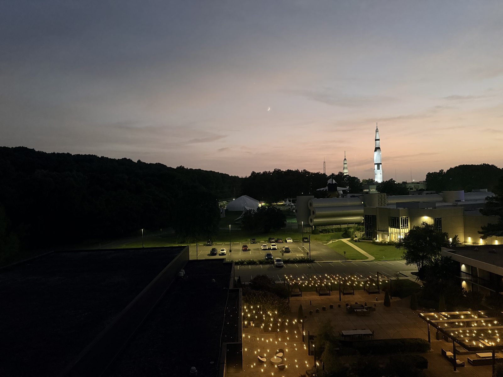 Twilight view of the illuminated Saturn V rocket with a crescent moon overhead